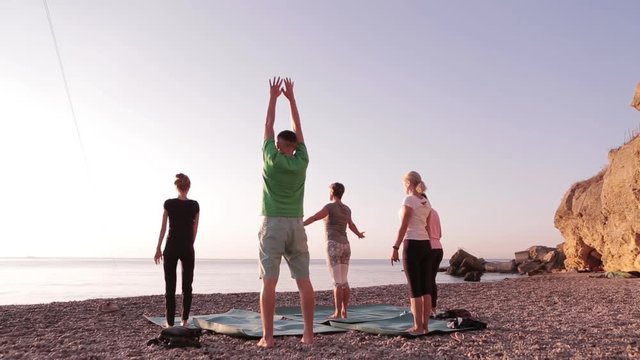 Yoga Class Group Adult Women And One Man Practice Yoga And Do Breathing Exercises With Instructor On The Beach At Sunrise. Wellbeing, Wellness, Fitness, Sport, Yoga And Healthy Lifestyle Concept, Full