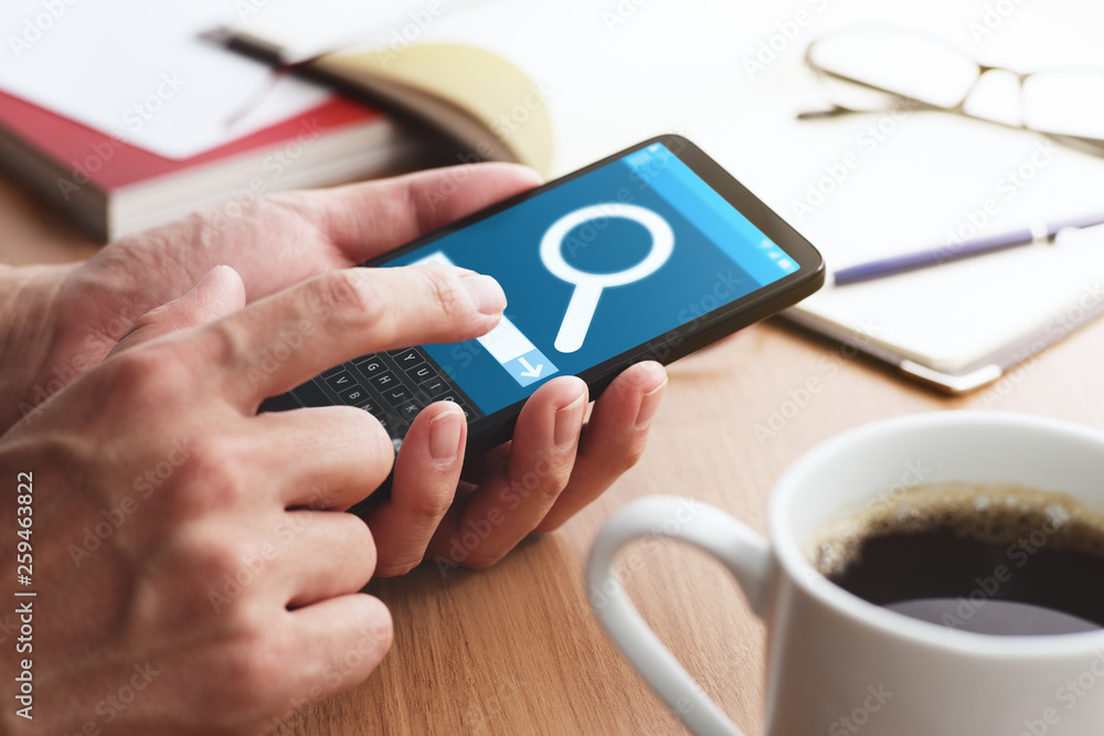 Poster closeup of male hands touching smartphone screen for internet search at table. magnifying glass icon