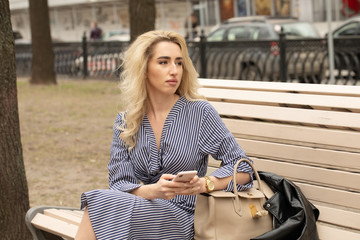 Young attractive girl using smartphone while sitting on a bench in the park