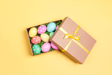 Easter eggs in a gift box on yellow background.