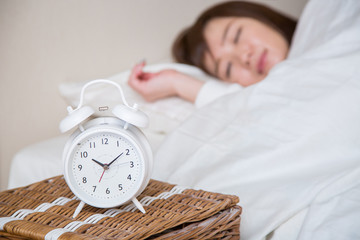 目覚まし時計で起きる女性（時計にピント）