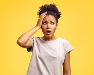 Stupefied girl holds hand on head, can't believe. Photo of african american girl wears casual outfit on yellow background. Emotions and Omg concept