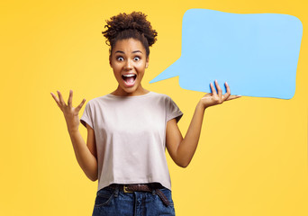 Overjoyed girl holds blue speech bubble board. Photo of african american girl wears casual outfit...