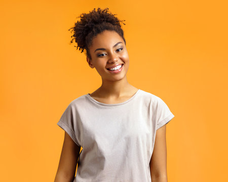 Cheerful girl laughs happily. Photo of african american girl wears casual outfit on orange background. Emotions and pleasant feelings concept.