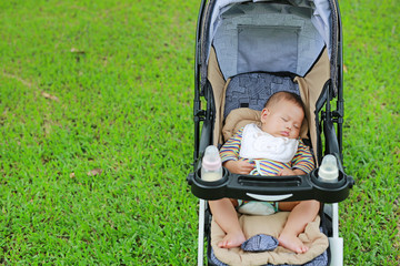 Asian baby boy sleeping in stroller on nature park.