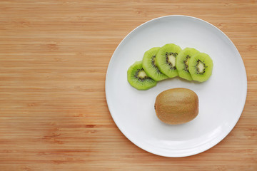 Kiwi fruit and sliced in white plate on wooden board background with copy space.