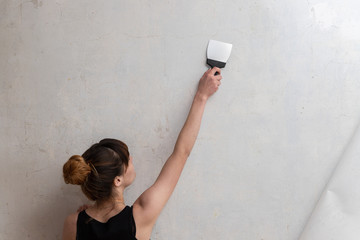 The girl makes the repair of the apartment. A woman leads a spatula on a concrete wall. Renovation of the apartment. Putty irregularities and cracks.