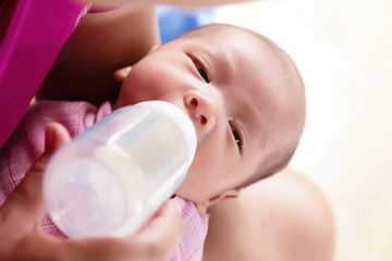 Mother feeding newborn baby boy with milk in nursing bottle.