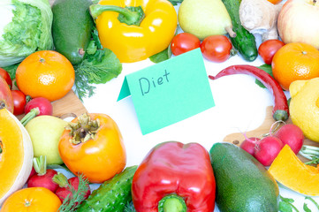 Vegetables and fruits closeup on wooden background. Mango, red pepper, lemon, cucumber, dill, tangerine, parsley. In the middle of the cutting Board and a piece of paper with the inscription diet