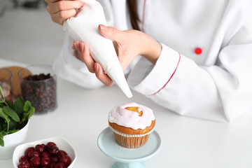 Young female confectioner decorating cupcake in kitchen