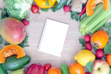 Vegetables and fruits closeup on wooden background. Mango, radish, yellow pepper, red pepper, lemon, cucumber, dill, tangerine, parsley. In the middle of the cutting Board and a piece of paper