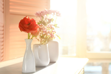 Vases with beautiful flowers on table in room