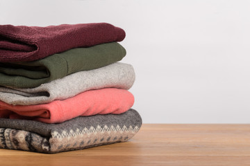 different sweaters on a wooden table on a light background. Autumn and winter clothes.