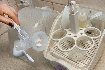 The process of safely removing feeding bottles and other items from a sterilizer using tongs. Close-up of sterilizer, used to disinfect baby bottles, teethers, pacifiers toys and other