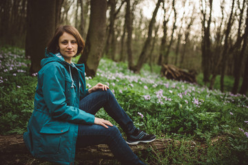 Toned photo of happy hiking middle-aged woman in blue jacket sitting and resting in evening spring forest