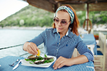Young woman presses lemon juice on an oyster. Beautiful young woman eating seafood in an outdoor...