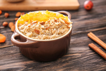 Pot with tasty sweet oatmeal on wooden table