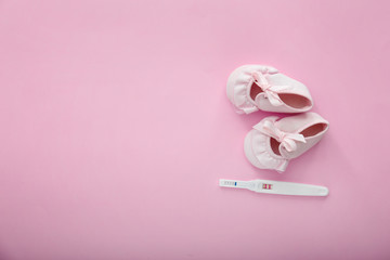 Pregnancy test and baby booties on color background