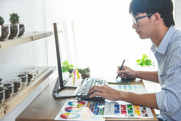 Image of male creative graphic designer working on color selection and drawing on graphics tablet at workplace with work tools and accessories in workspace