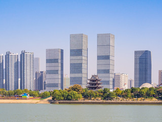 View at the bank of Xiang river in Changsha, the main city of Hunan Province, China. There are tall modern buildings, as well as traditional pavillion standing beside. Asian cityscape on a sunny day.