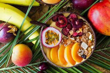 Smoothie bowl and exotic fruits on tropical palm leaves. Top view