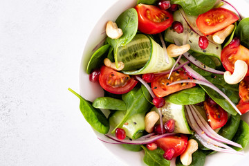 Top view of healthy classical vegetable fresh salad of spinach, tomato, cucumber, onion, cashew nuts, pomegranate and sesame with olive oil dressing on white plate and white background. Diet menu.