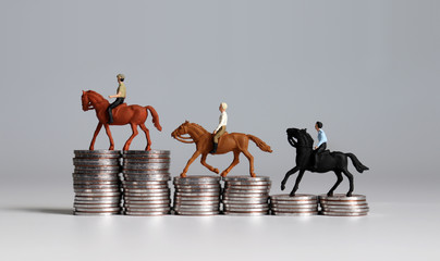 Miniature men riding horse on coin stacks. 