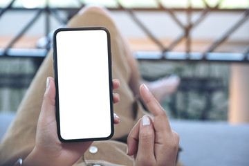 Mockup image of a woman holding black mobile phone with blank white desktop screen while laying down in living room with feeling relaxed