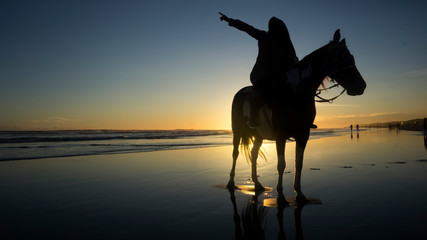 silhouette of muslim women who are riding horses on the beach with the atmosphere of the sunset