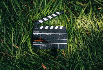 Black clapperboard with film lying on the grass in the nature outdoors. Directing and of amateur cinema movie. Creative concept. Retro vintage photo.