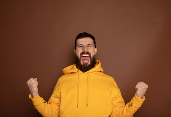 Happy young man celebrating his success over yellow background 