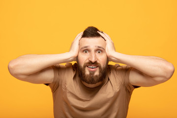 Indoor shot of amazed excited man doesn`t believe his success, keeps hands on head, stares at...