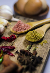 Close up of fennel powder in wooden spoon surrounded with various asian spices and ingredients on wooden deck.