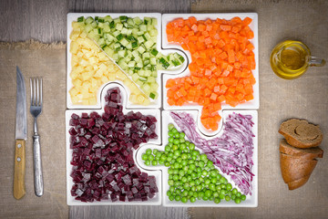 .Raw vegetables carrots, peas, onions, cucumber, potatoes, beets cut into cubes lie on puzzles in the form of puzzles and gather in a single large dish.