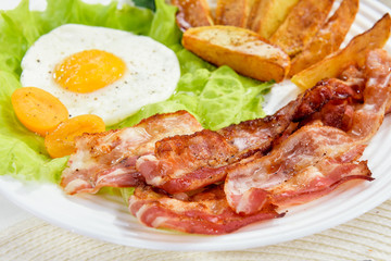 Fried bacon with French fries and a delicate egg, close-up.