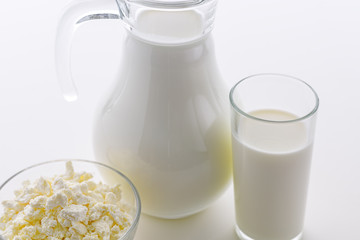 Fresh milk in a glass poured from a jug with a bowl of cottage cheese on a white background. Dairy products for breakfast are very healthy.