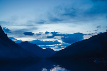 Fototapeta na wymiar Amazing blue silhouettes of mountains on dusk. Dawn sky reflected in mountain lake. Wonderful atmospheric highland landscape. Beautiful ripples on lake water with twilight bright. Scenic mountainscape