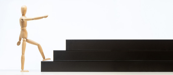 Omino di legno sale le scale, punta dritto all'obiettivo per raggiungere il suo traguardo. Concetto di determinazione e raggiungimento. Sfondo bianco, scale nere.