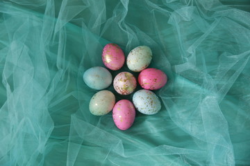 Colorful Easter eggs in a turquoise veil in the shape of a flower with copy space for text. Flat lay. Top view. Easter background.
