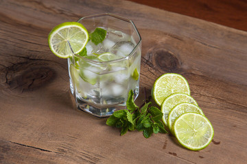 Summer cocktail mojito in glass, sliced lime and mint on wooden background..