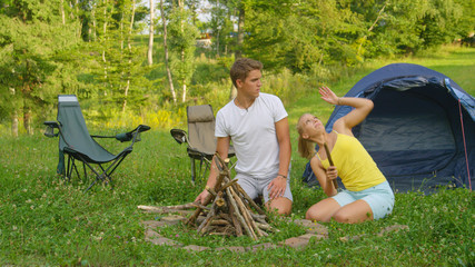 Man and woman on fun camping trip trying to swat the bugs flying around them.