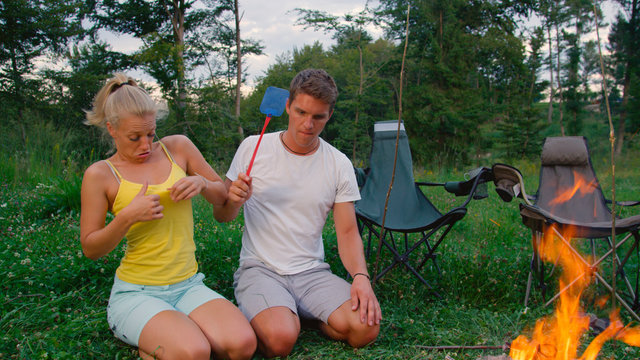 CLOSE UP: Couple Tries To Swat Pesky Bug Annoying Them While Sitting By Campfire