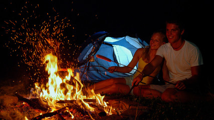 CLOSE UP: Happy camper striking fire while roasting sausages with girlfriend.