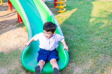 Fototapeta na wymiar Asian kid playing slide at the playground under the sunlight in summer, Happy kid in kindergarten.