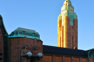 Fototapeta premium Helsinki, Finland. View Of Statues On Entrance To Helsinki Central Railway Station in shadows and sun Illuminated clock tower in back ground.