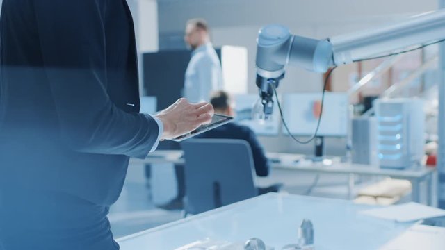 Stylish Female Industrial Robotics Engineer Uses Tablet Computer with CAD Software and to Manipulate and Program Robot Arm for Lifting Moving Objects. Technology Research Facility for Machine Learning