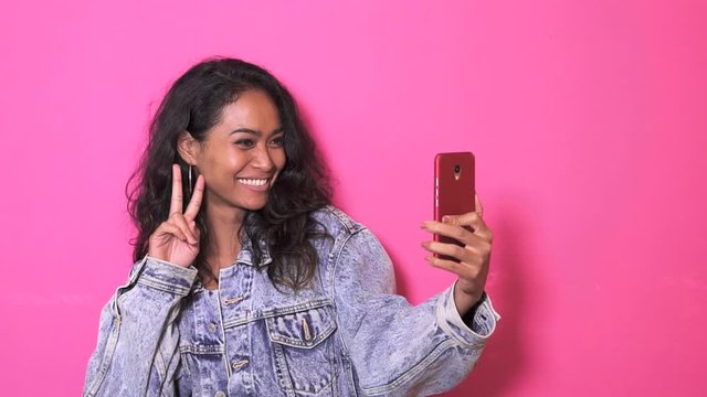 footage of expressive asian girl taking selfies on her mobilephone with pink background