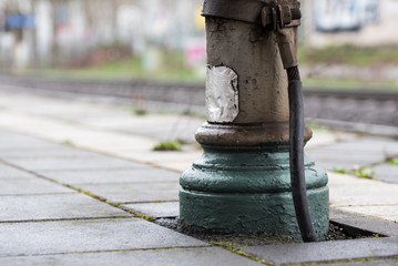 old metallic post with a big cable or wire and green and grey painting standing at a railwaystation and blurred background