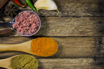 Close up of turmeric powder in wooden spoon with other blurred spices and asian ingredients on wooden deck.