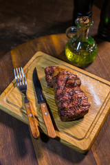 Juicy medium Beef Rib Eye steak on wooden board with fork and knife herbs spices and salt.